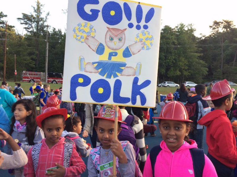 Pok students on playground. One holding a "go Polk" sign