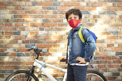 A boy wearing a mask stands by a bicycle