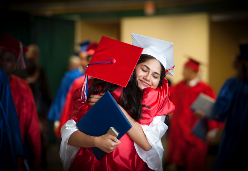 Two high school graduates in graduation growns hugging