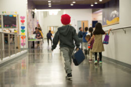student walking down the hall holding lunch box with back to camera