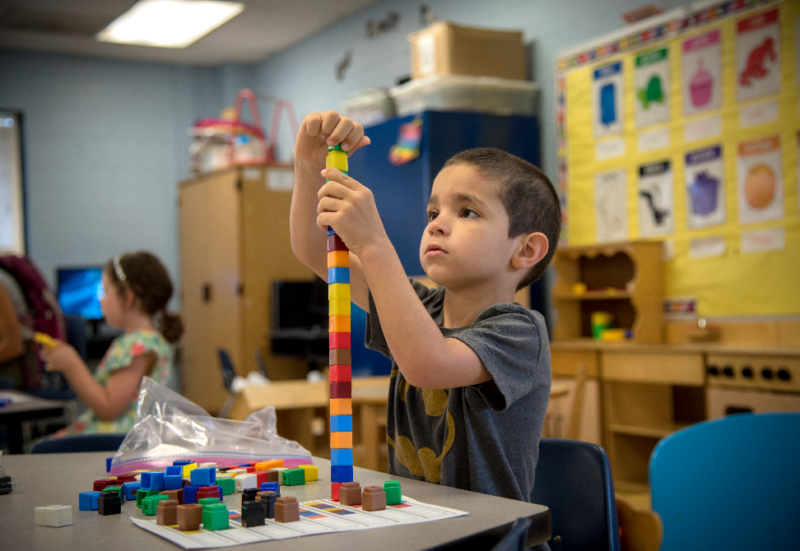 Kindergarten student stacking small colorful blocks on desk