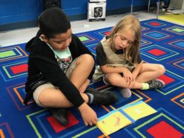 elementary school students reading book together on classroom carpet