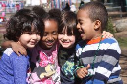 group of four pre-school aged kids hugging and smiling