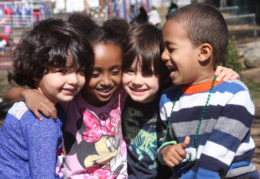 four preschool students hugging on a playground