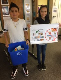 male student holding a recycle bin with female student holding a recycling poster