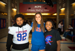 Three TC athletes stand together under the athletic hall of fame banner