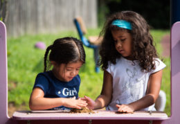 Two elementary school-aged girls playing with dirt on an outdoor surface
