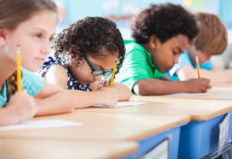 Multi-ethnic elementary school children writing in classroom.