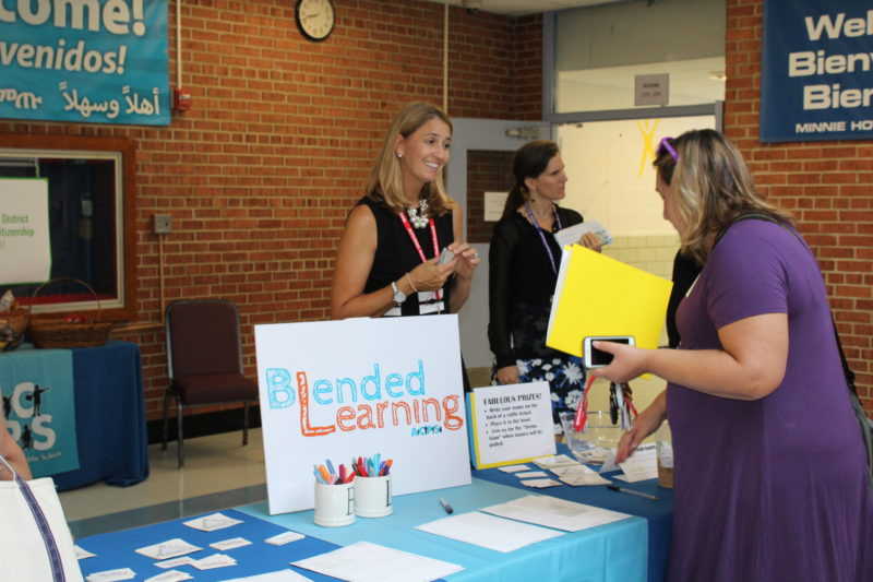 Two women talking over Blended Learning Camp materials table.