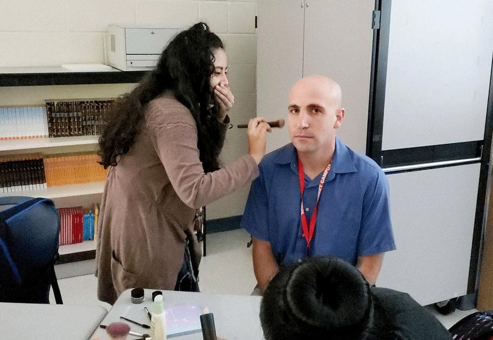 student applies makeup to teacher Gabe Elias