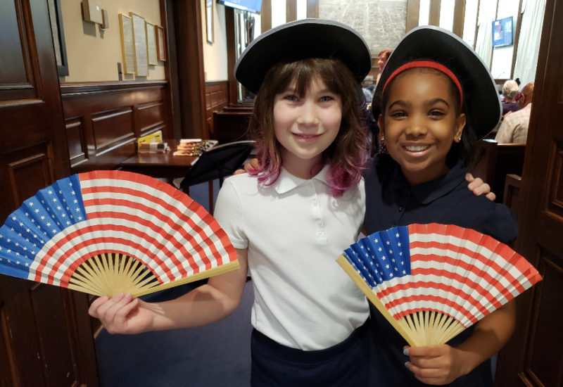Two elementary school-age girls holding flag fans