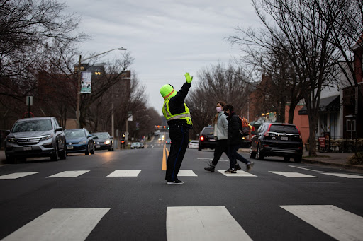 A crossing guard holds up her hand to stop traffic in the center of a crosswalk early in the morning.