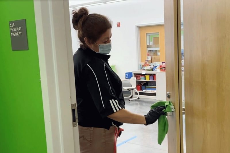 A female custodian wipes the handle of a classroom door