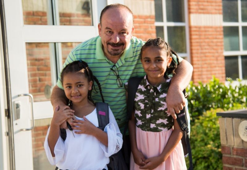 father with two young daughters outside of school