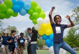 A fourth grade female student poses with a gallon of water on top of her head in front and arch of balloons on the track field