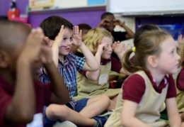 Kindergarteners sitting on the floor singing The Wheels on the Bus