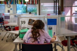 The back of a high school student sitting at a desk writing