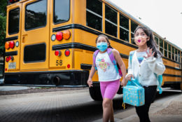 Two girls with masks walk to school after getting off the school bus