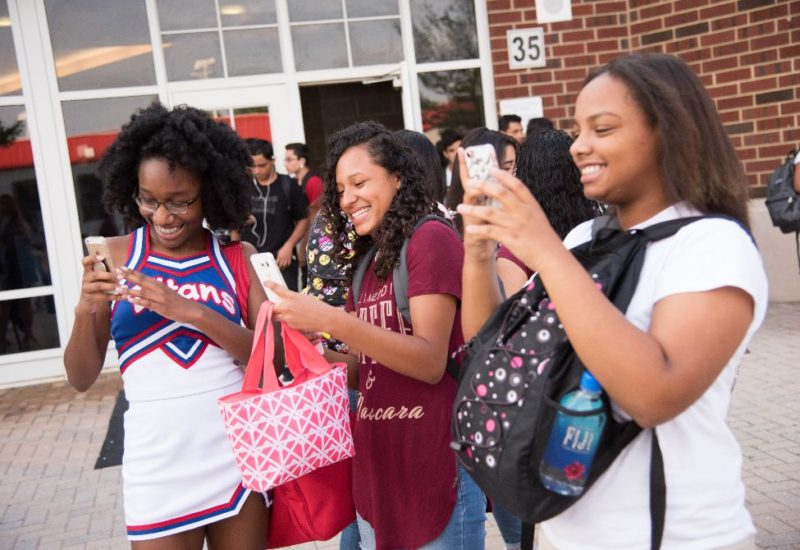 Three high school girls smiling and taking pictures on smartphones