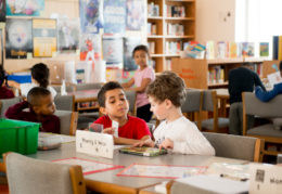 two elementary boys reading book at table