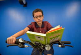 young male student reading a book on stationary bike
