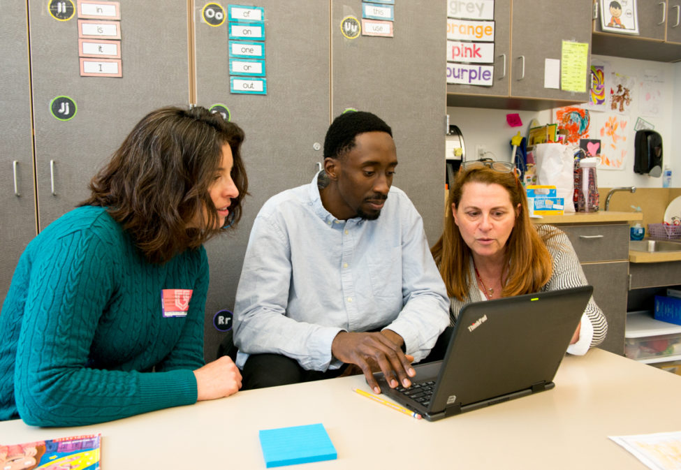 Three teachers gathered around a laptop in classroom