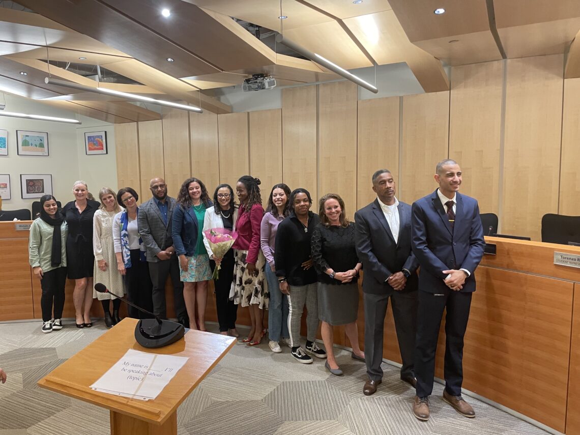 The school board with student representatives and Superintendent Kay-Wyatt gather around the dais and Kay-Wyatt poses with flowers.